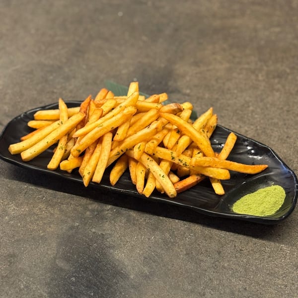 Golden french fries seasoned with herbs, served on a black plate with a side of green powder.