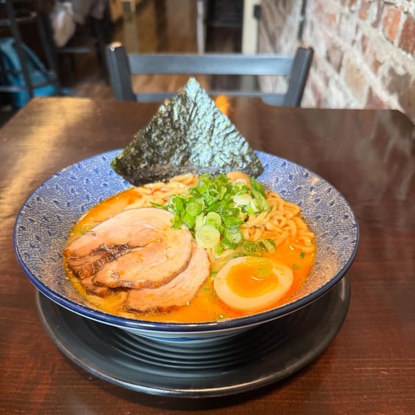 A bowl of HINODEYA ramen with pork, egg, green onions, and nori on a wooden table.