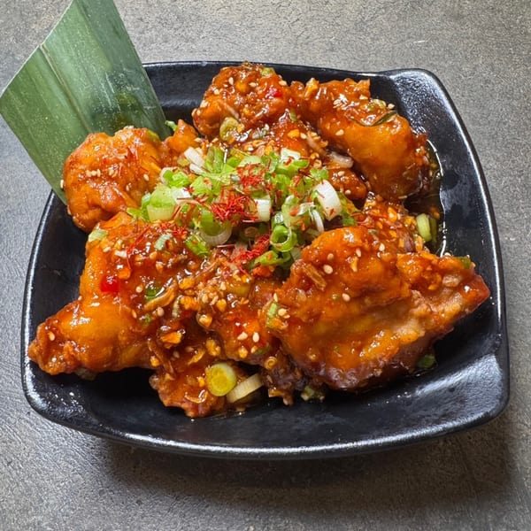 HINODEYA Ramen's fried chicken, glazed with sauce, topped with green onions and red spices.