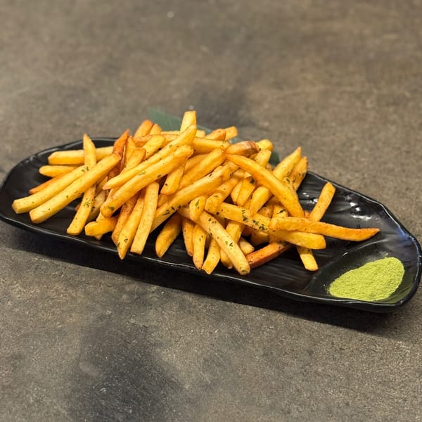 Golden french fries seasoned with herbs on a black plate, with a side of green matcha powder.