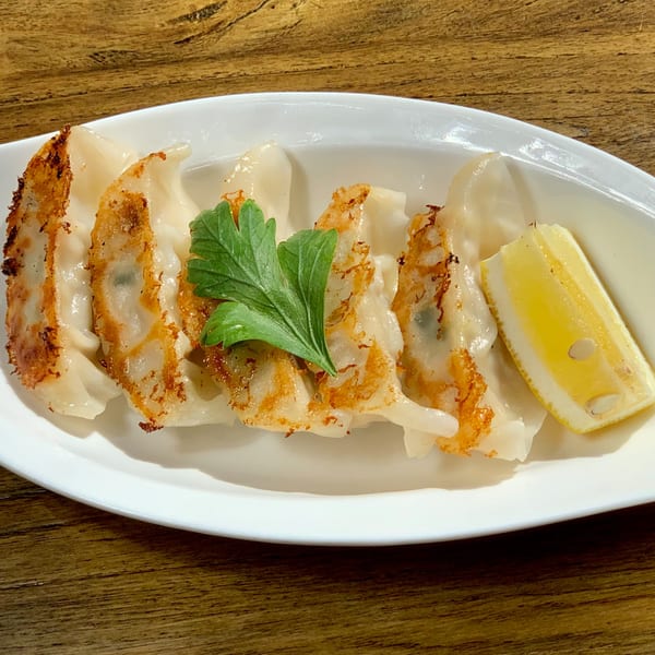 HINODEYA Ramen's gyoza, pan-fried and served with a lemon wedge and parsley on a white plate.