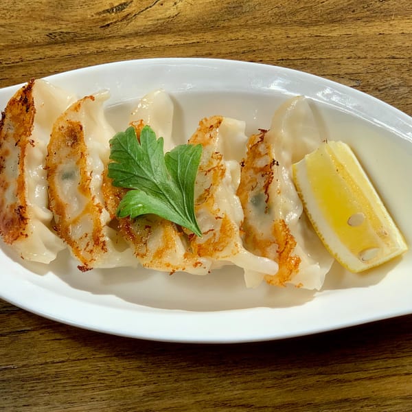 Pan-fried gyoza with crispy bottoms, garnished with parsley and a lemon wedge on a white plate.