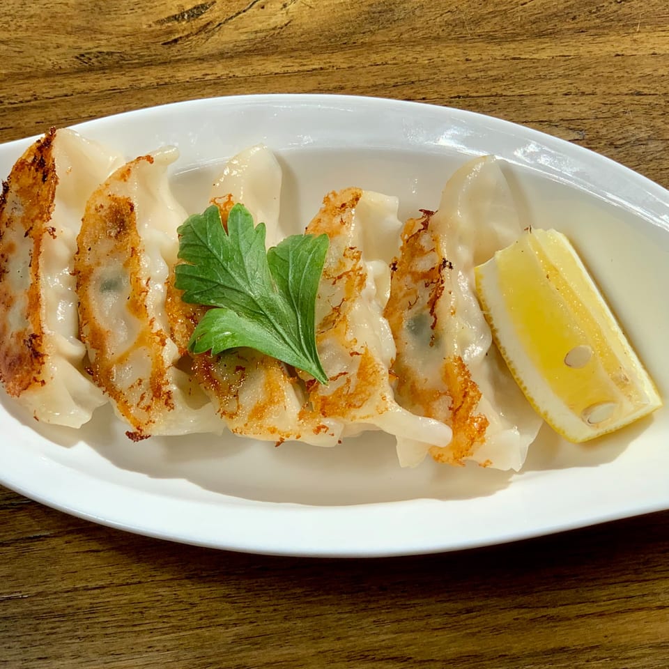 Pan-fried gyoza with crispy bottoms, garnished with parsley and a lemon wedge on a white plate.