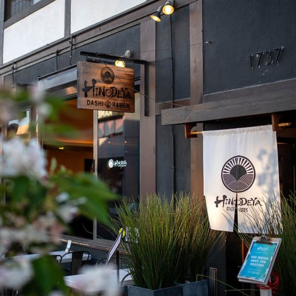 Exterior of HINODEYA Ramen restaurant with wooden and fabric signs, and outdoor seating.